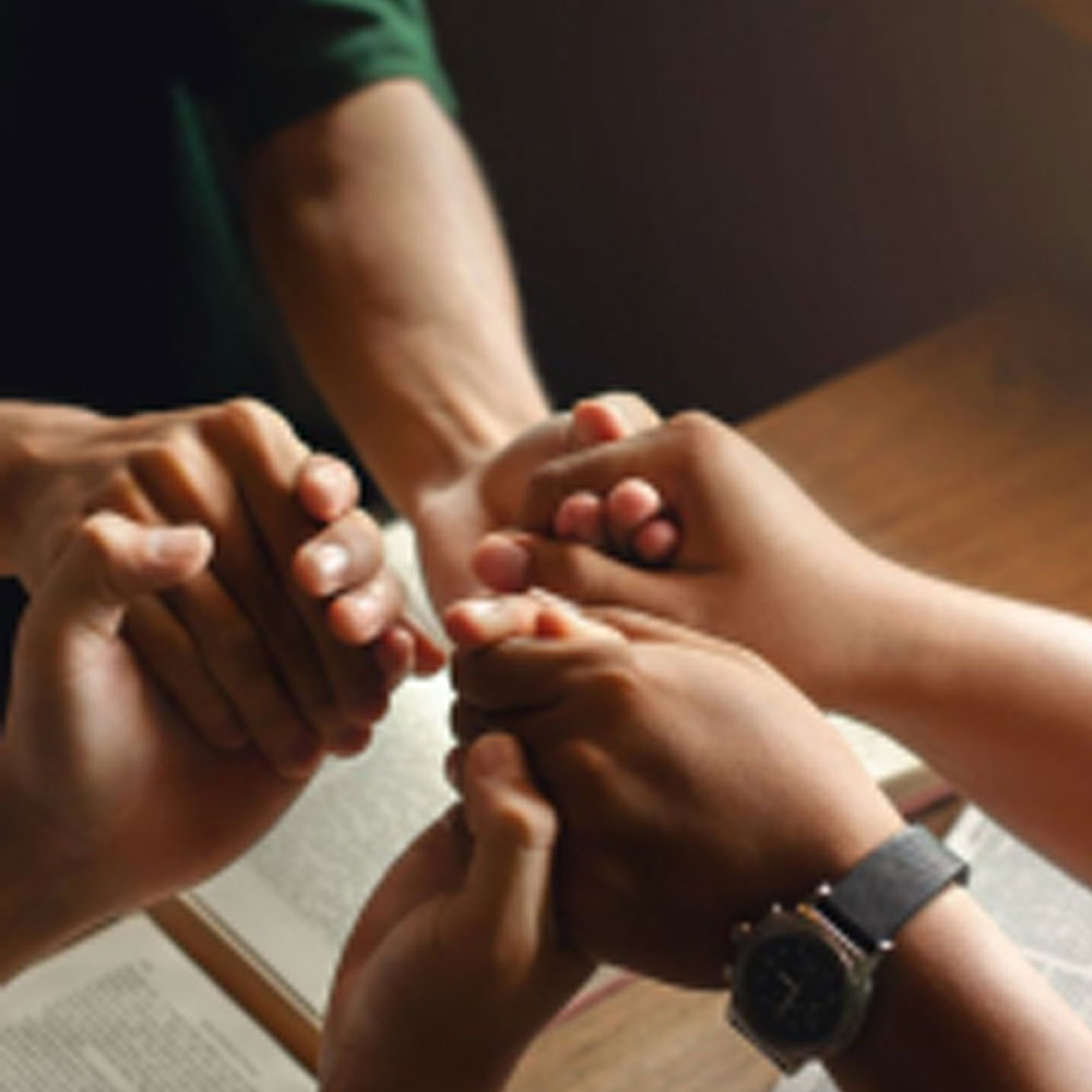 3 people holding hands praying